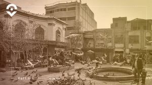 یک حوض قدیمی در گوشه ی چپ تصویر با تعداد زیادی کبوتر در اطرافشو ساختمانهای قدیمی در گوشه راست تصویر